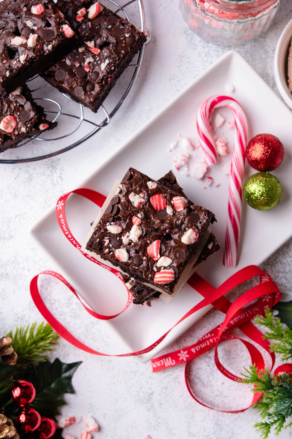 A serving tray with a large candy cane, two ornaments, and a stack of peppermint brownies with merry Christmas ribbon around them.