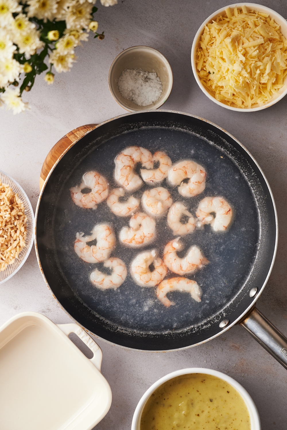 A large skillet with boiling water cooking shrimp.