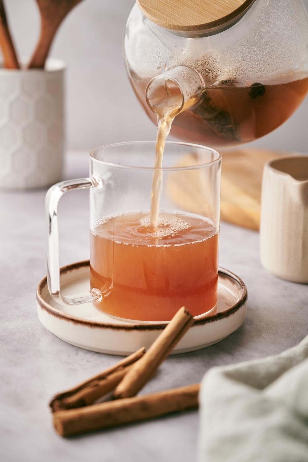 A small teapot with chai tea is being poured into a clear mug.