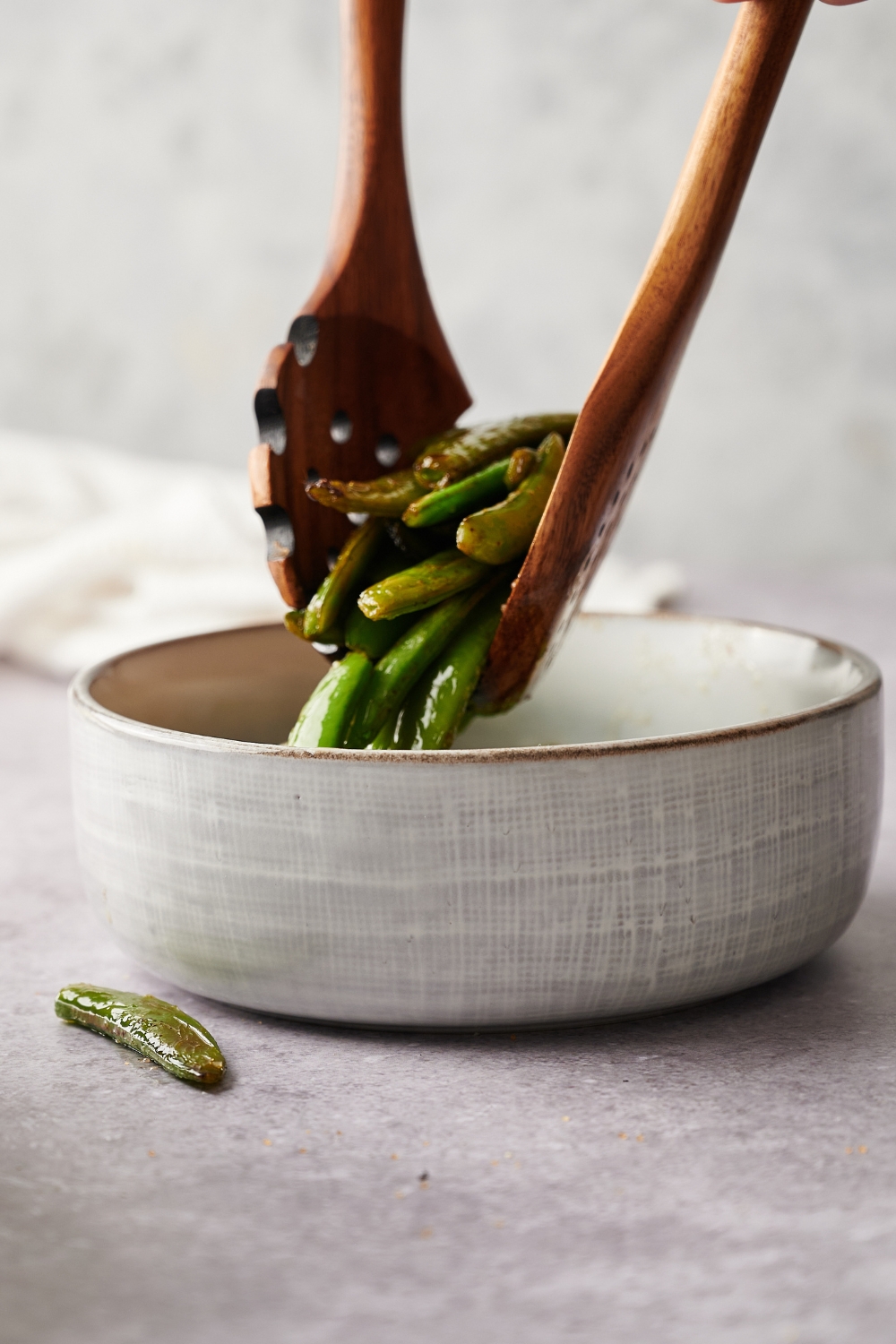 A small bowl with tongs serving a scoop of cooked buttery sugar snap peas.