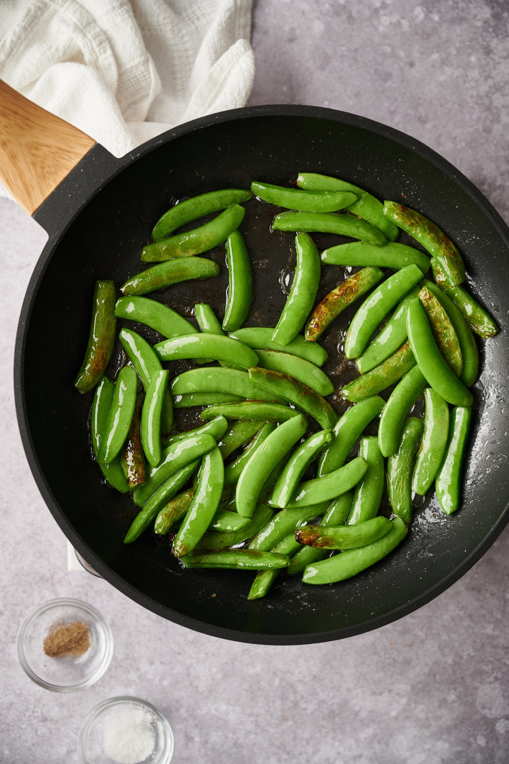 A hot pan with sugar snap peas being cooked in butter.