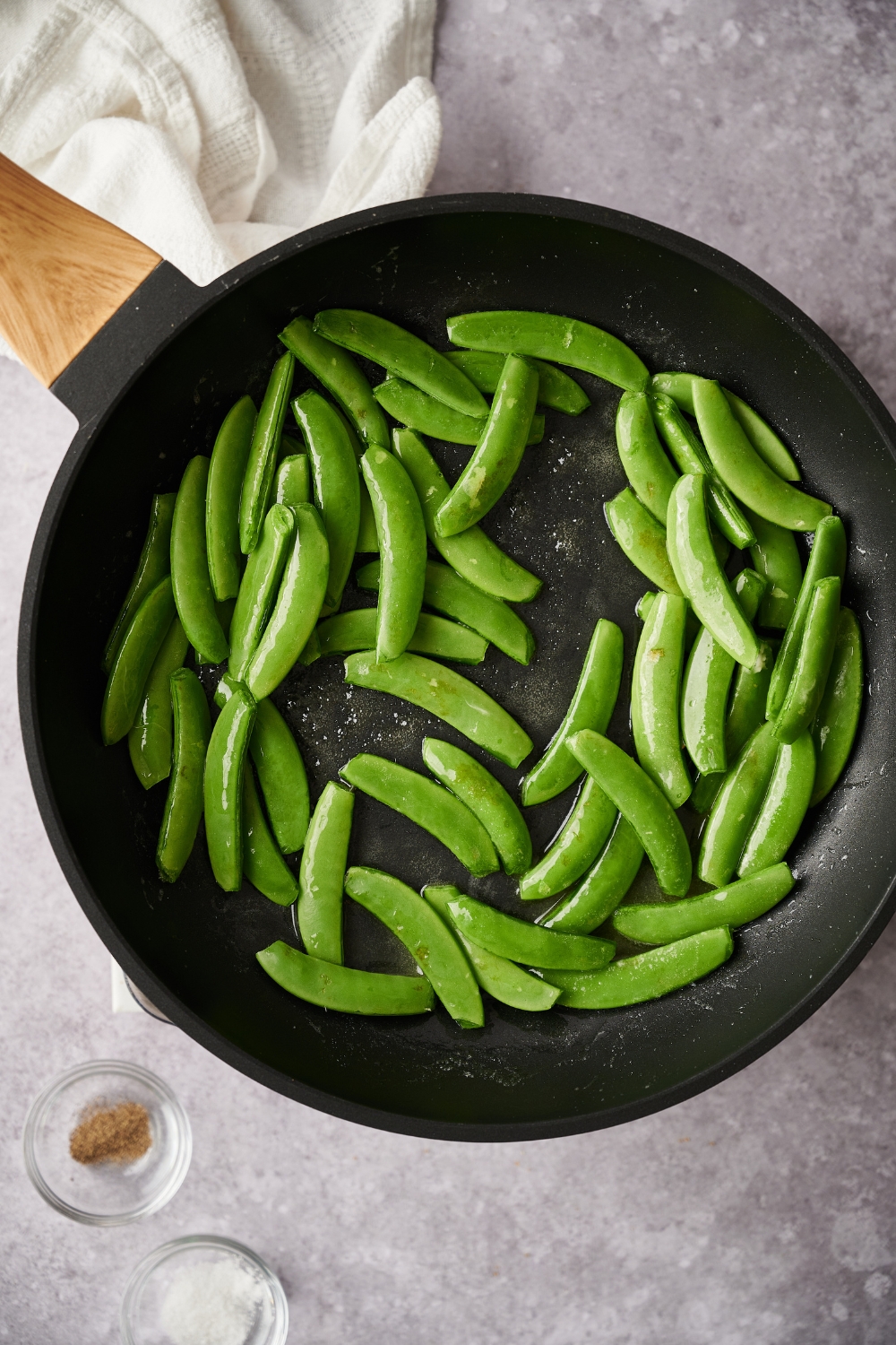 A hot pan with sugar snap peas being cooked in butter.