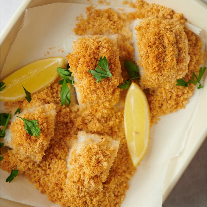 Bread crumbs on top of four haddock fillets in a parchment lined baking dish.