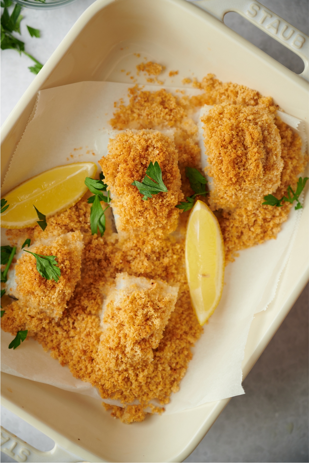 Bread crumbs on top of four haddock fillets in a parchment lined baking dish.