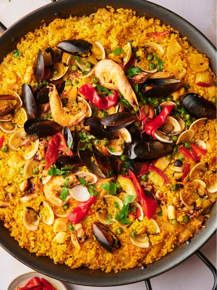 A mixture of seafood on top of yellow rice in a large skillet.