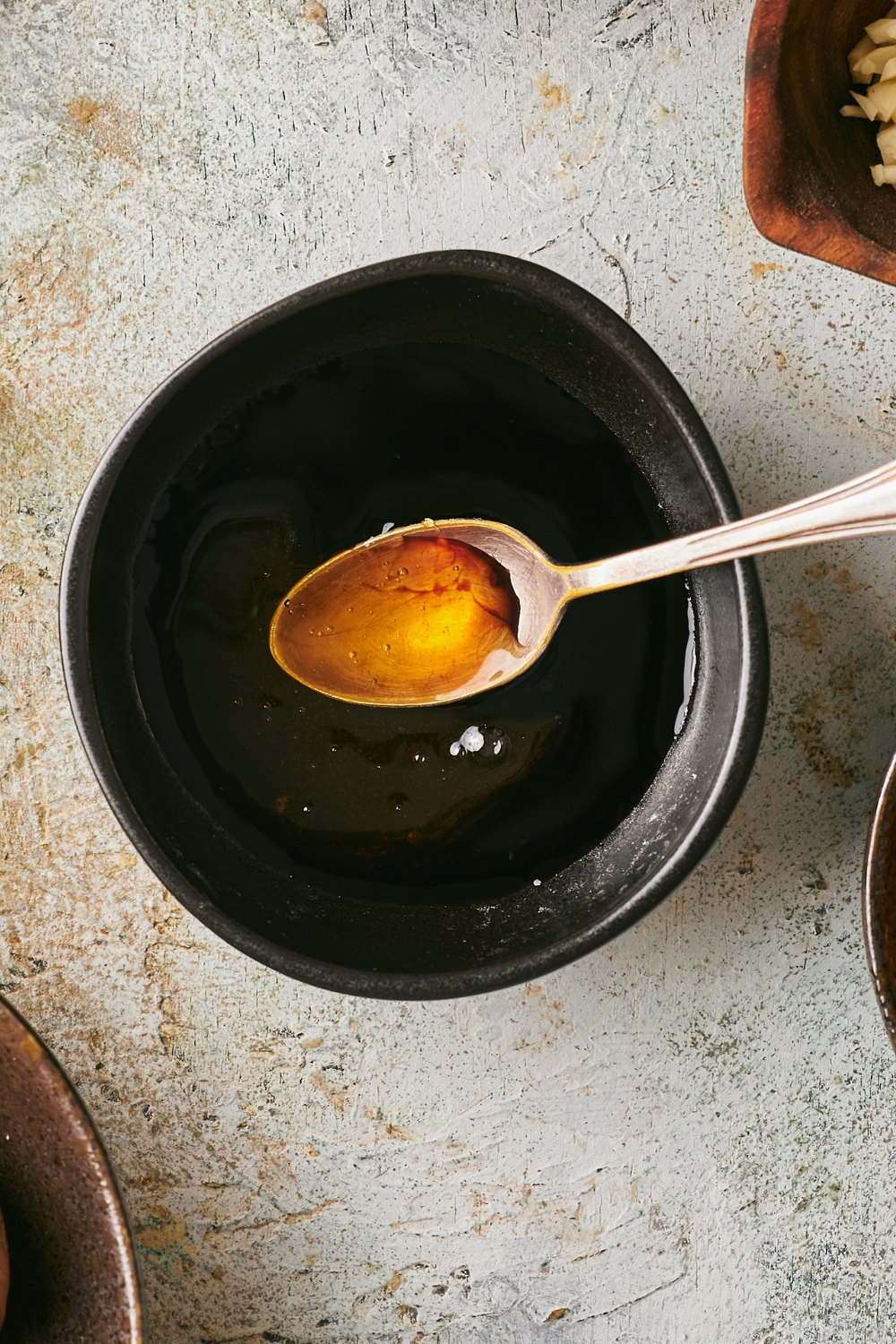 A spoon with a honey sauce on it above a bowl filled with the sauce.