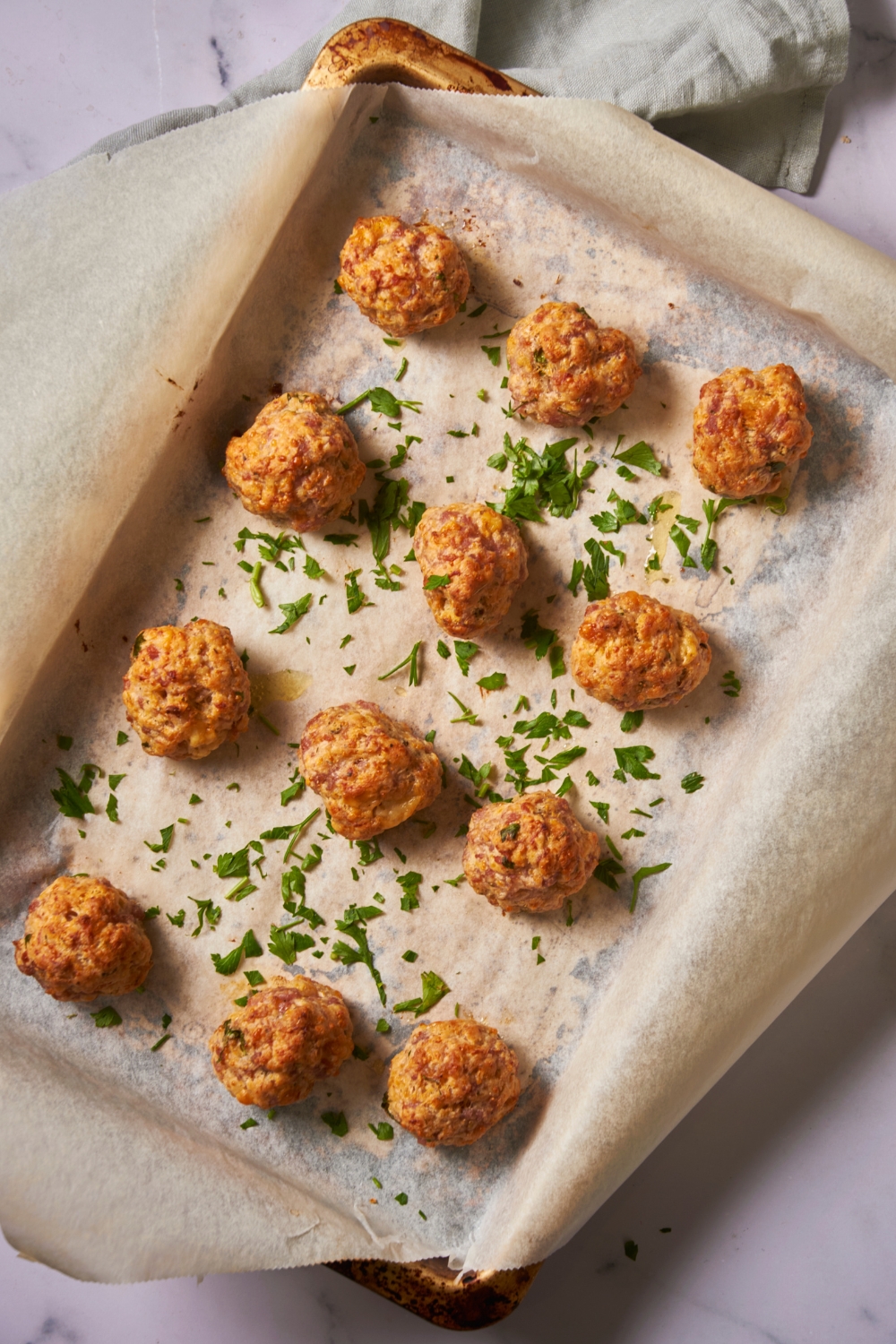 Baking sheet lined with parchment paper with freshly baked sausage balls topped with fresh parsley.