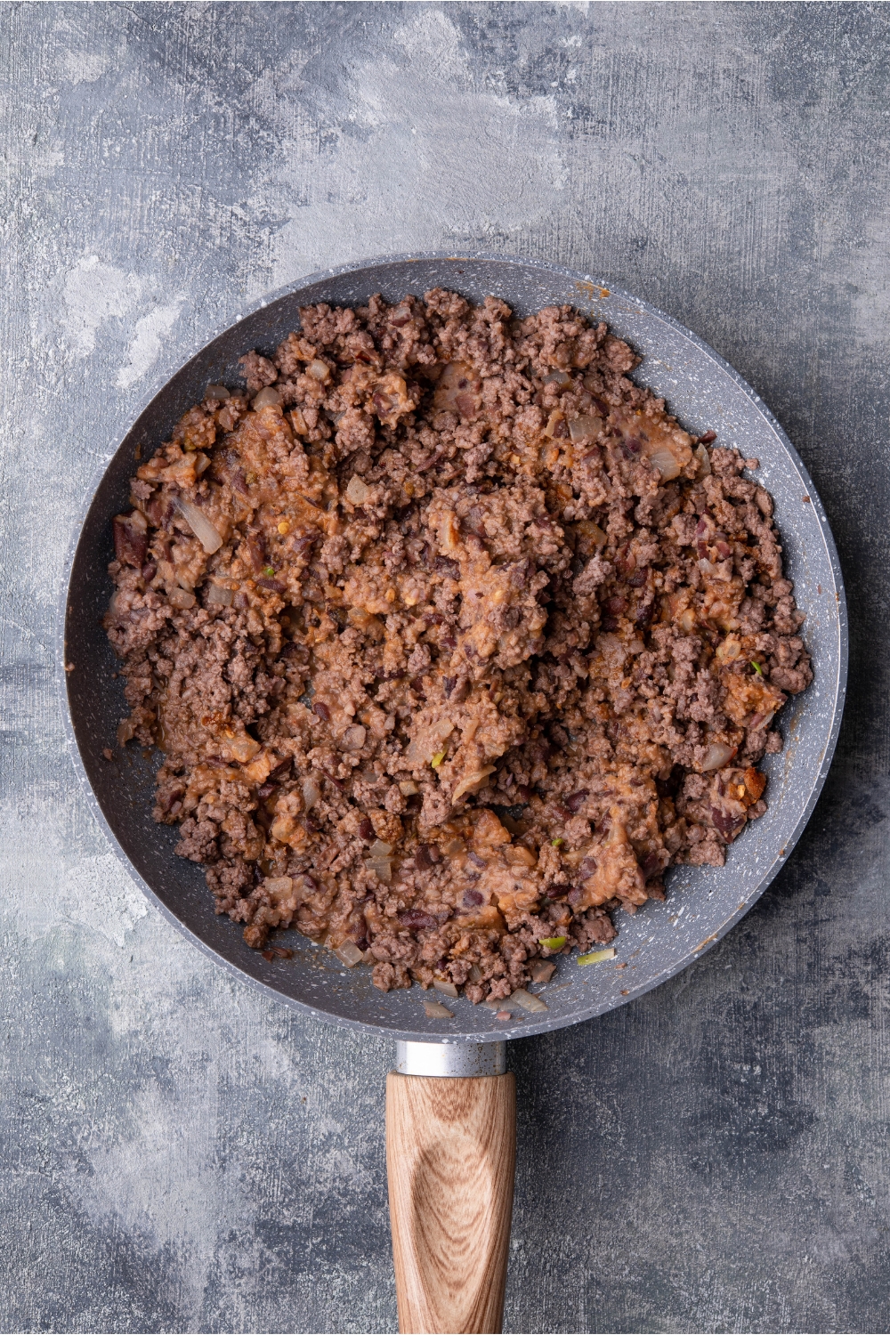 Skillet filled with seasoned ground beef and refried beans.
