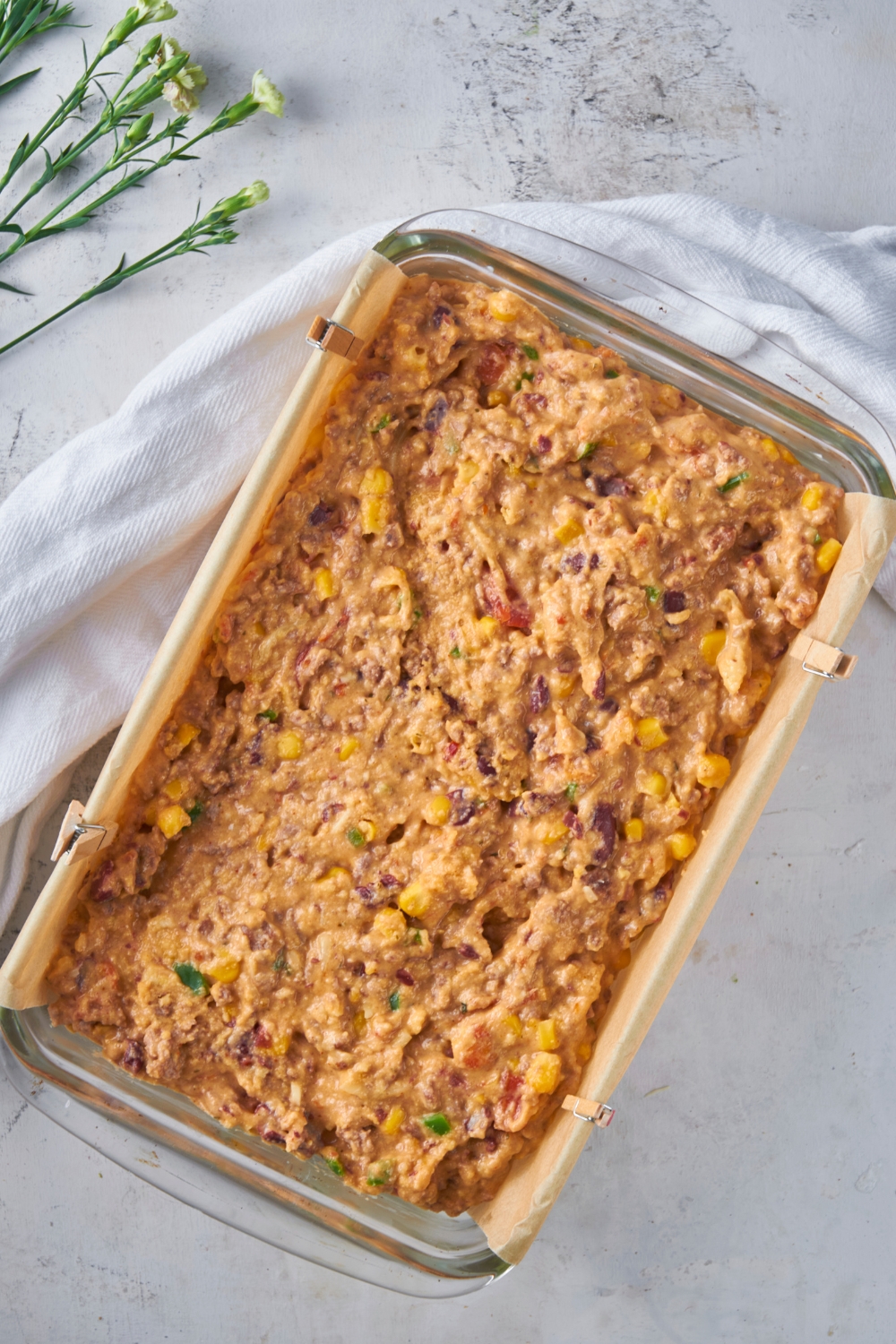 Clear baking dish lined with parchment paper filled with unbaked cowboy cornbread casserole.