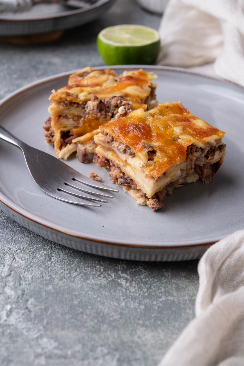 Two slices of burrito casserole on a blue plate with a fork on the plate.