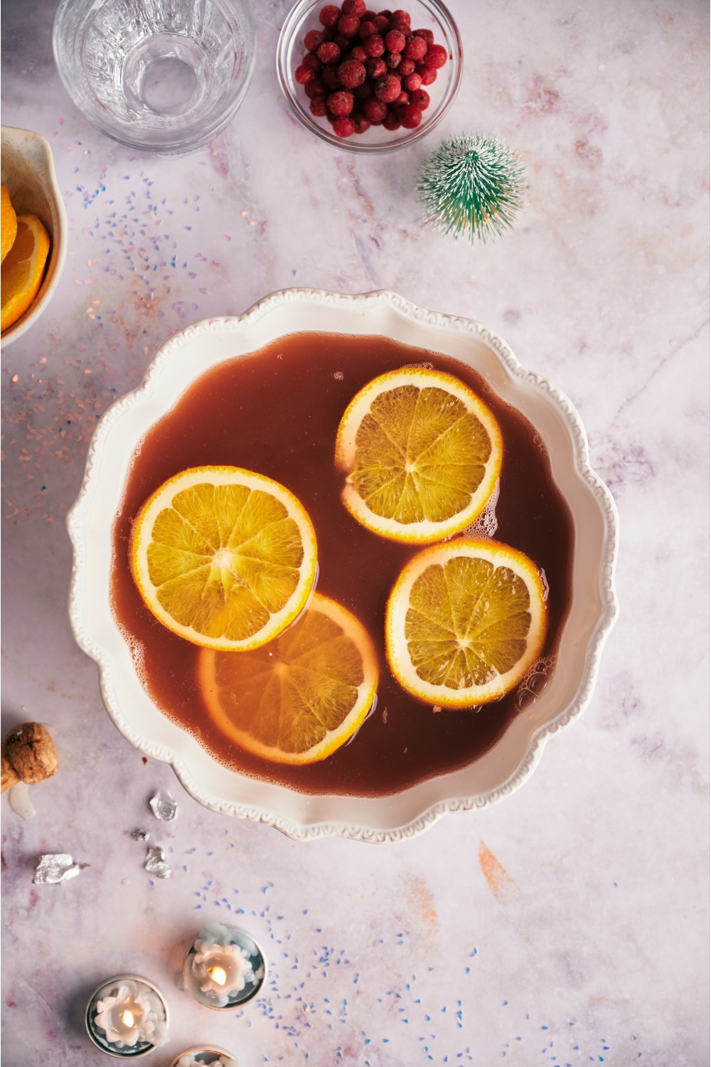 Large white punch bowl filled with holiday punch and orange wheels.