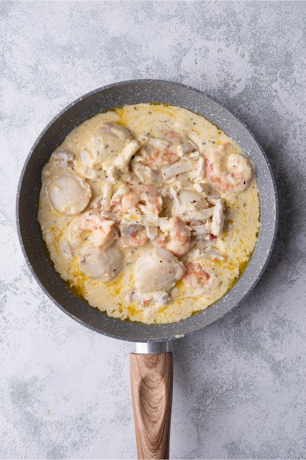 Skillet filled with scallops, shrimp, and crab meat in a seasoned cream sauce.