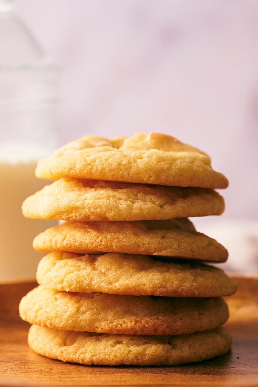 A stack of white chocolate macadamia nut cookies and a jar of milk behind it.