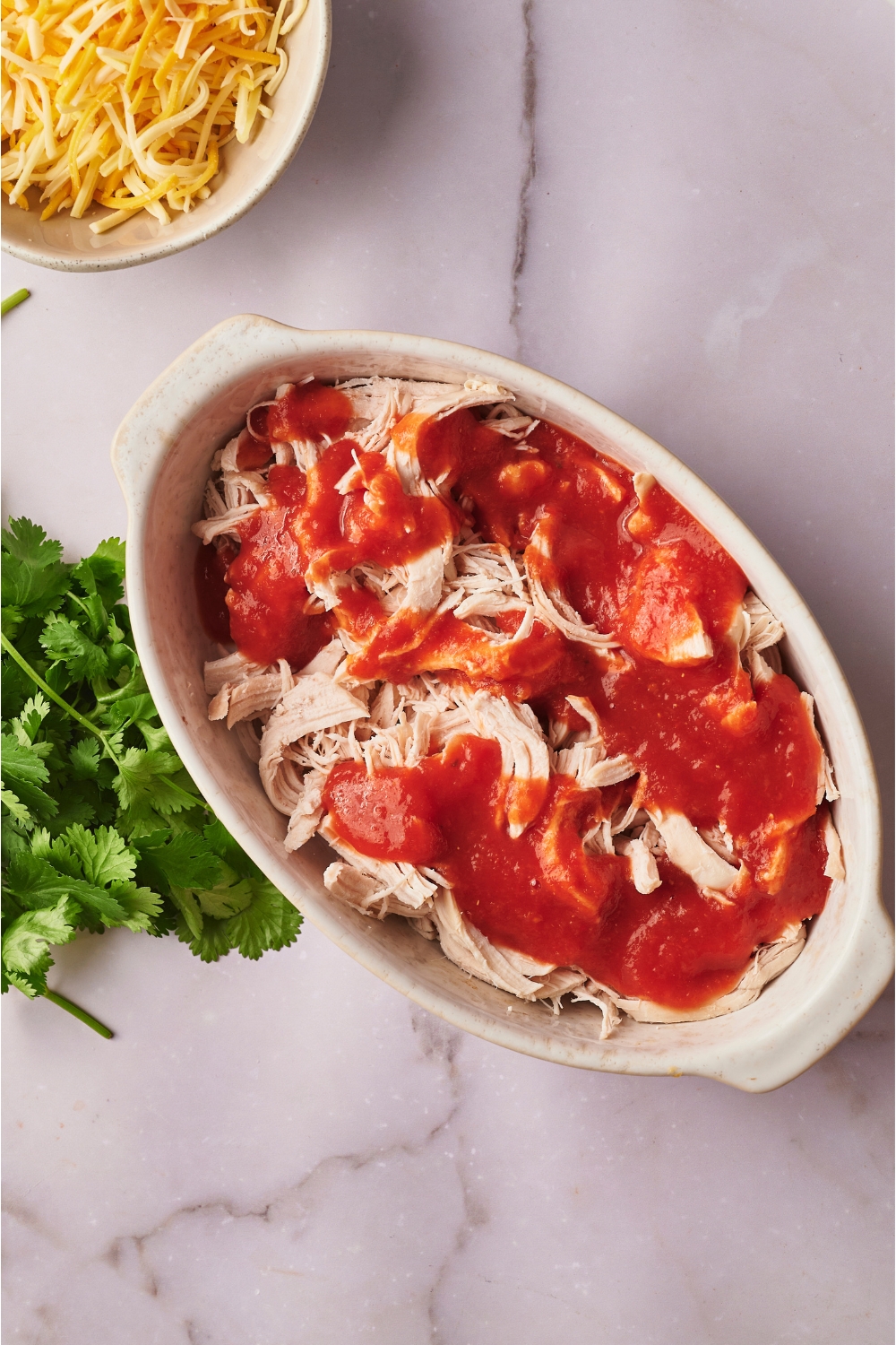 A white casserole dish filled with shredded chicken and red sauce.