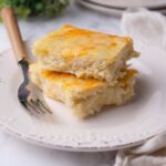 A stack of two squares of hash brown casserole on a plate with a fork next to it.