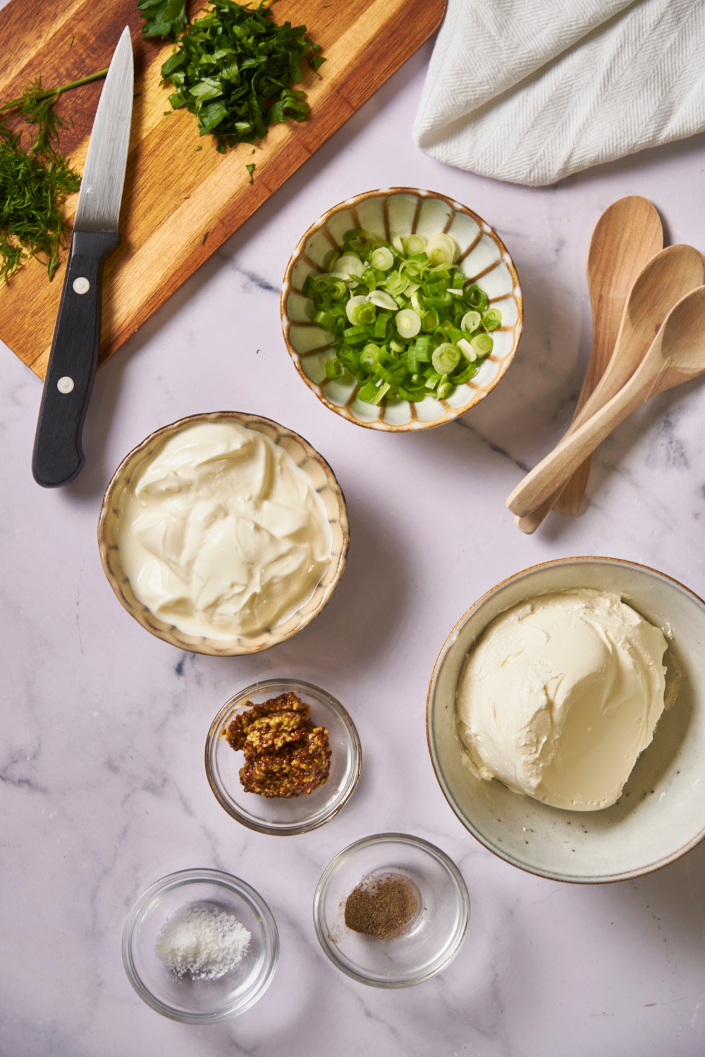 An assortment of ingredients including bowls of diced green onion, sour cream, cream cheese, and spices.