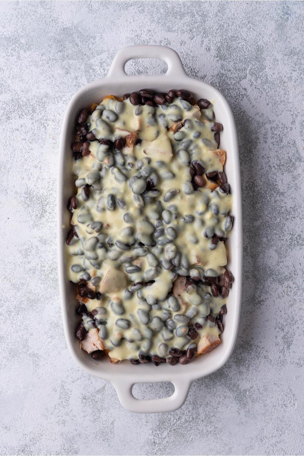 White baking dish filled with black beans, chicken and a creamy sauce.