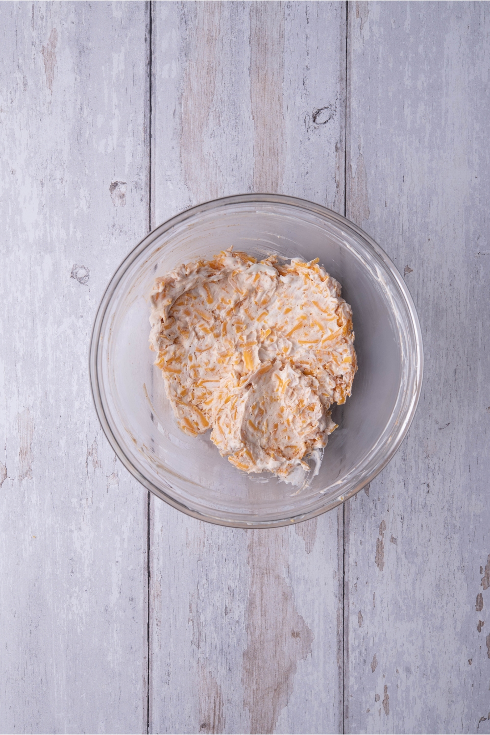A clear bowl filled with a cream cheese and shredded cheese mixture.