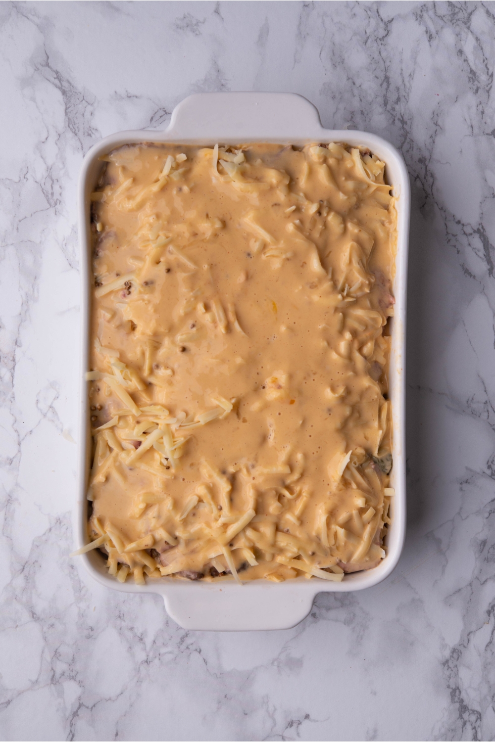 Unbaked Reuben casserole covered in a creamy sauce mixture in a white baking dish.