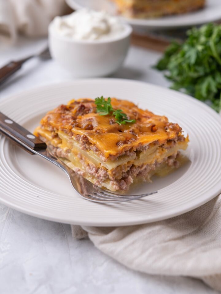 Single serving of hamburger potato casserole on a white plate with a fork on the plate.