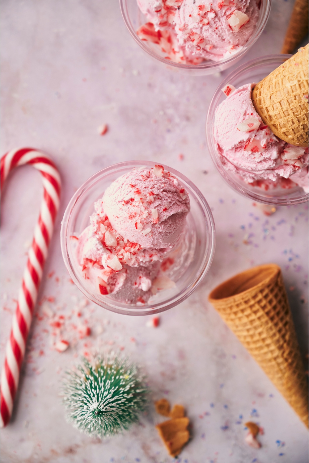 Peppermint ice cream in clear serving bowls, each topped with crushed candy canes and one topped with an ice cream cone.