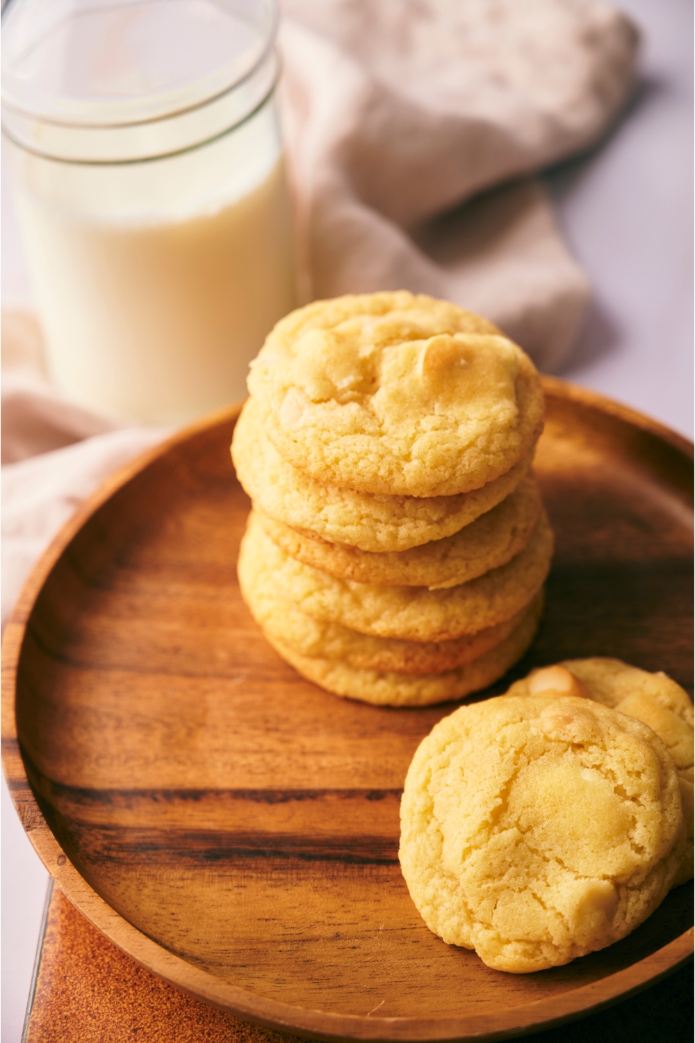 A stack of cookies on a wood plate that's on top of a wood board with a jar of milk next to them.