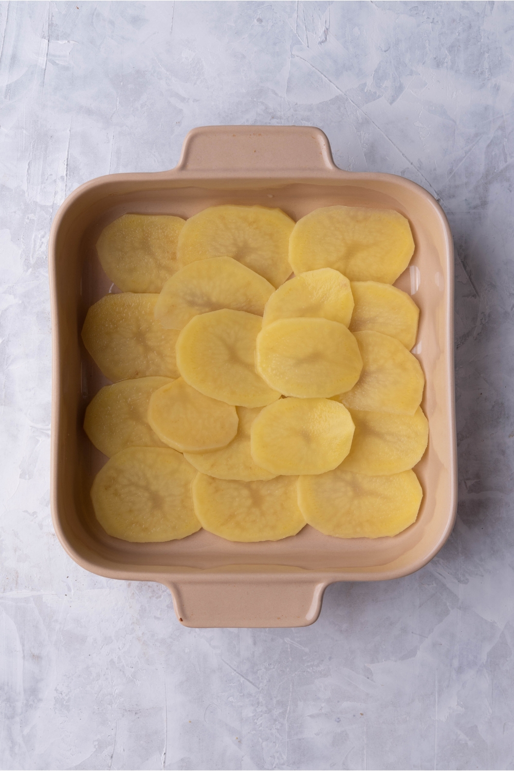 Brown baking sheet with a layer of thinly sliced potatoes.