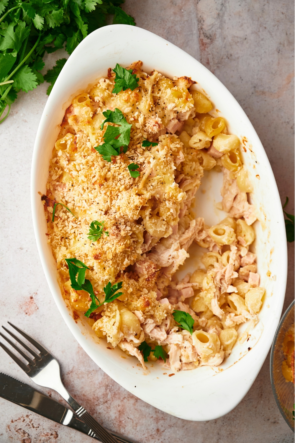 Chicken cordon bleu casserole in a white casserole dish with half of the casserole scooped out, next to a fork and knife.