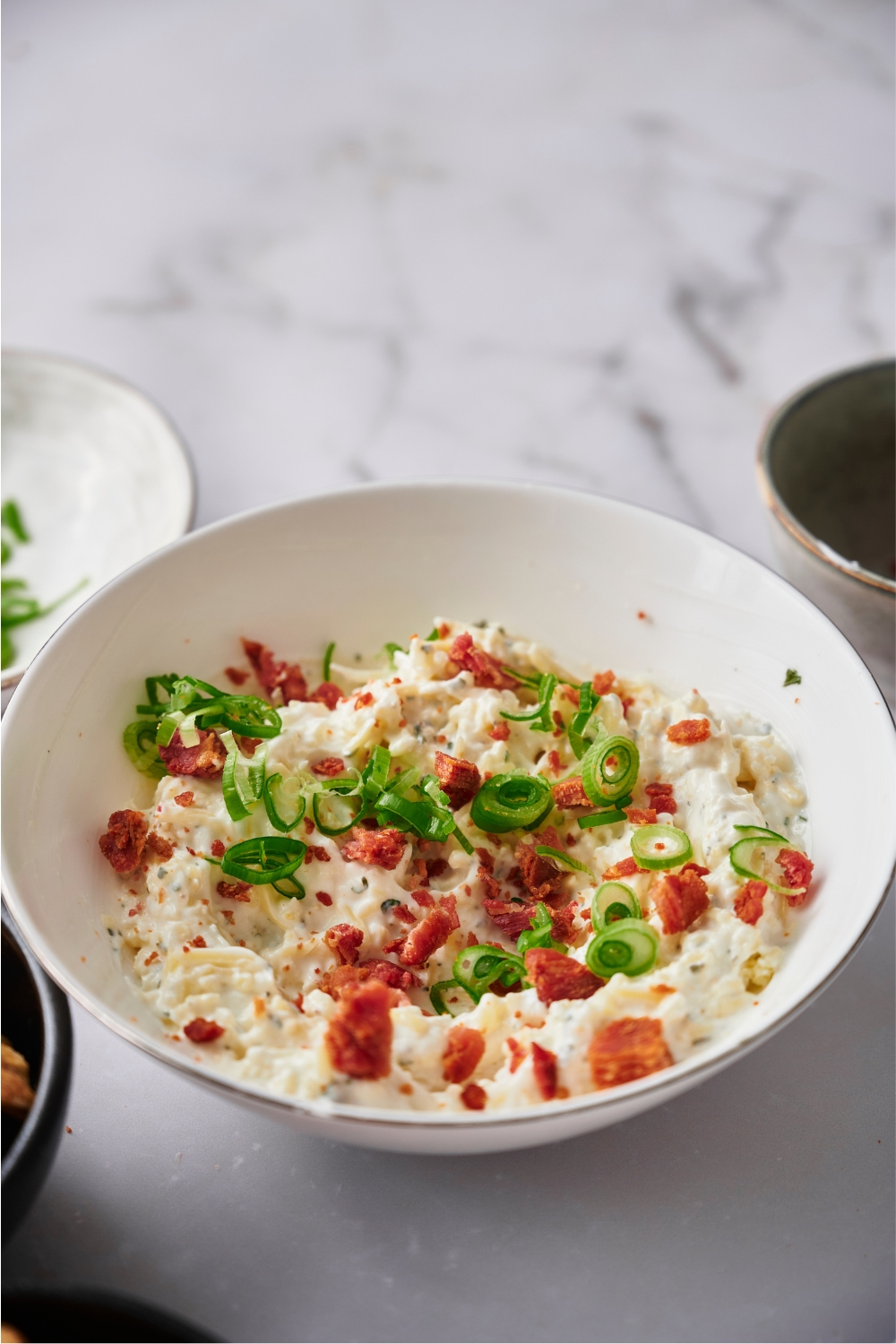 Crack dip in a white serving bowl topped with bacon bits and green onion.