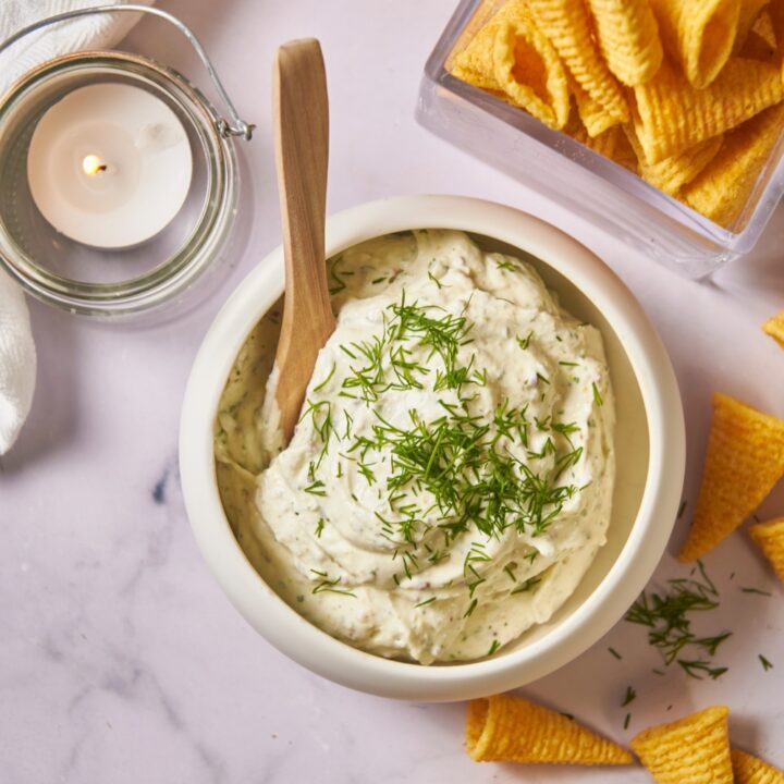 Overview of a white serving bowl with cream cheese dip and a bowl overflowing with chips.