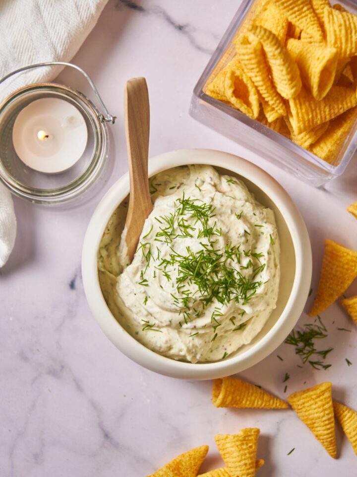 Overview of a white serving bowl with cream cheese dip and a bowl overflowing with chips.