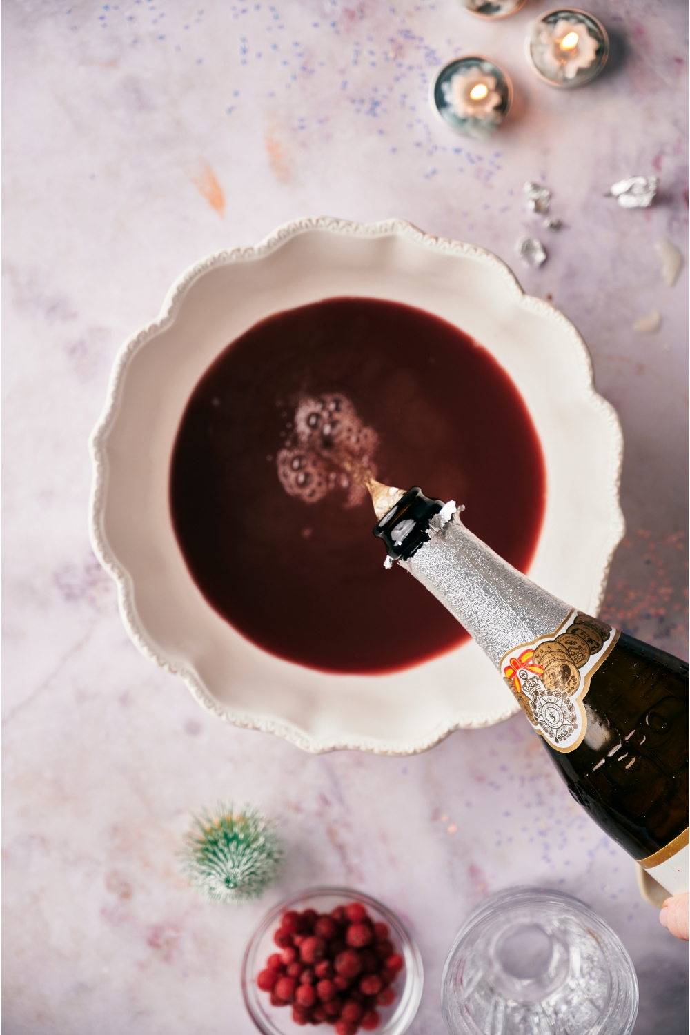 A bottle of sparkling juice being poured into a punchbowl filled with cranberry juice.