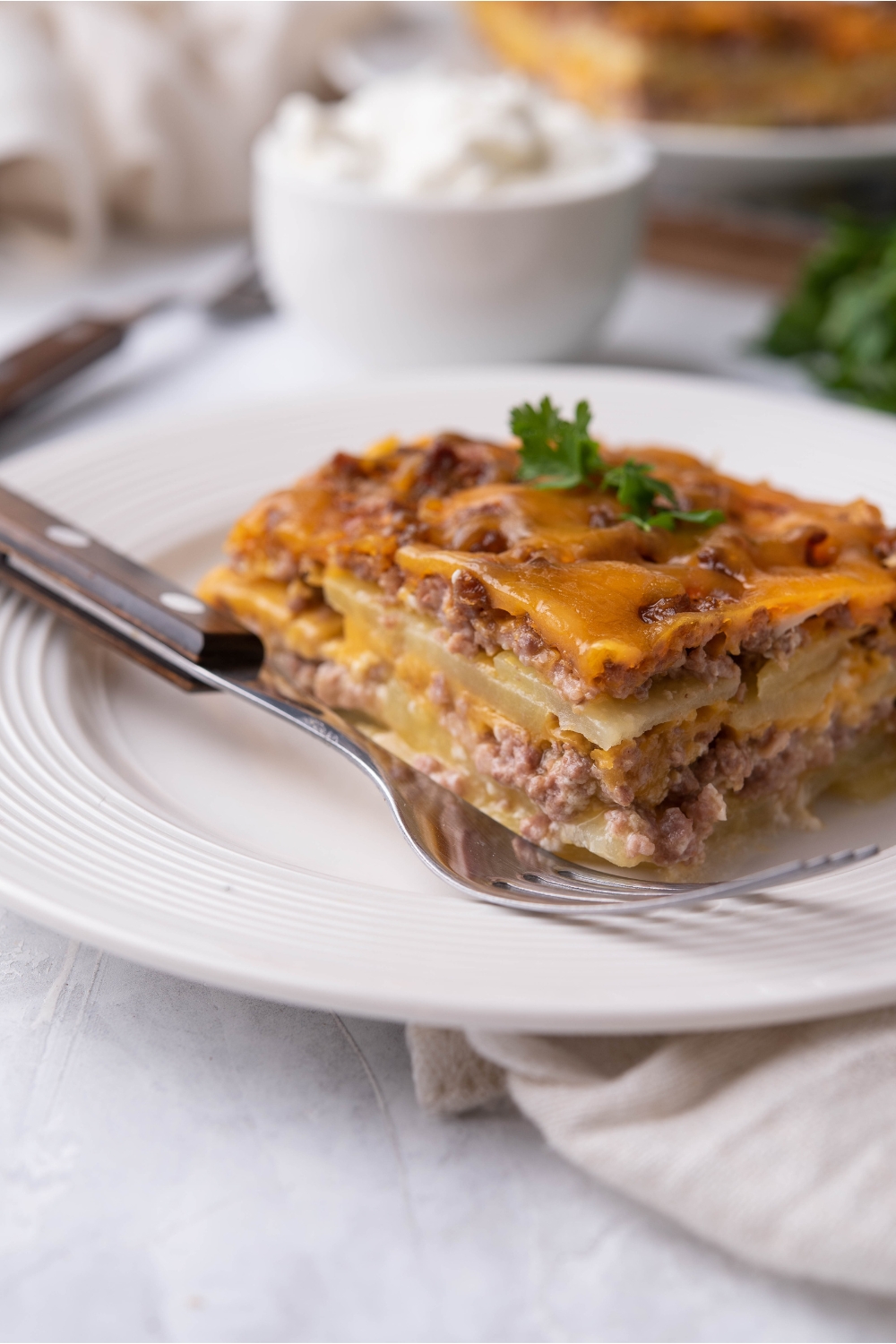 Single serving of hamburger potato casserole on a white plate with a fork on the plate.