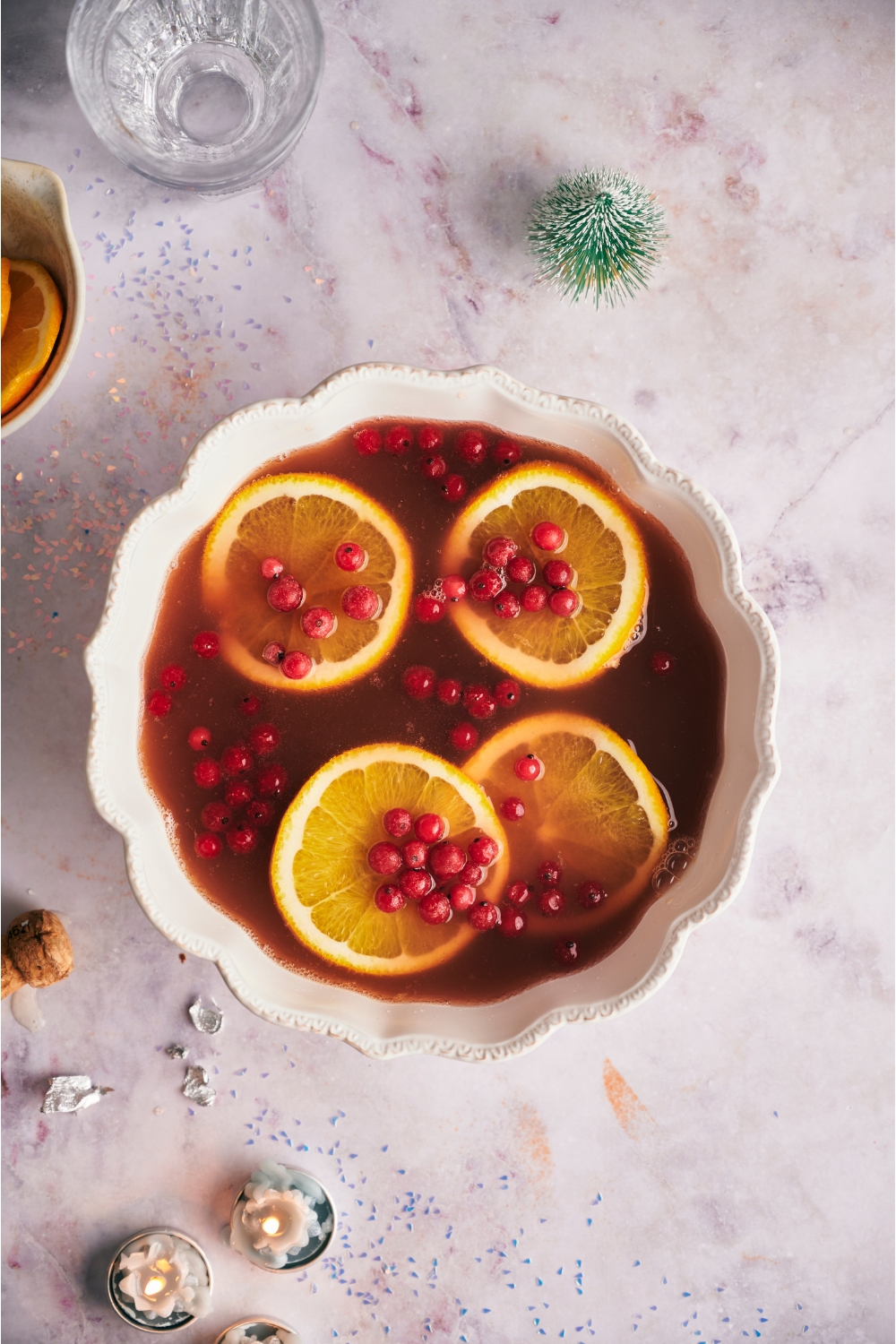 Large white punch bowl filled with holiday punch, orange wheels, and cranberries.