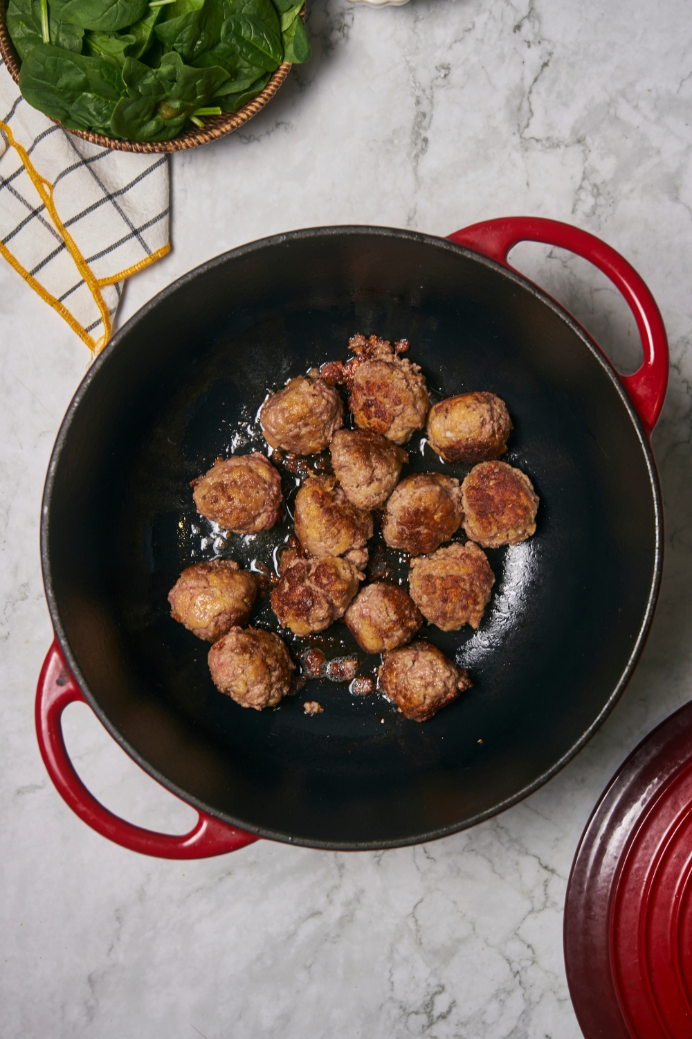 Red Dutch oven filled with browning meatballs.