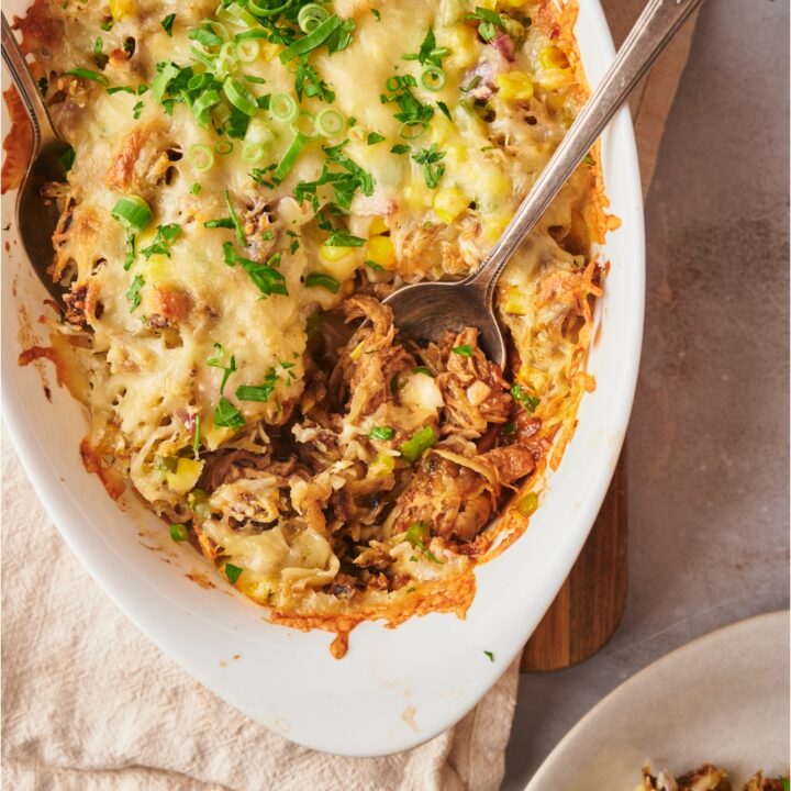 Pulled pork casserole with two serving spoons and a serving scooped out onto a white plate.