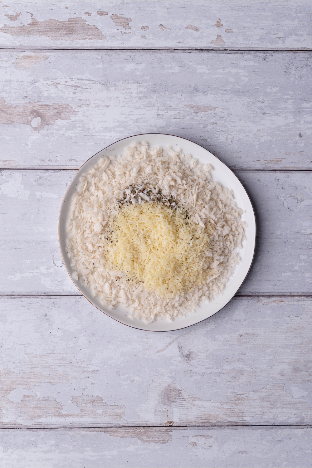 A white plate filled with bread crumbs, parmesan cheese, and spices. These ingredients have not been mixed together.