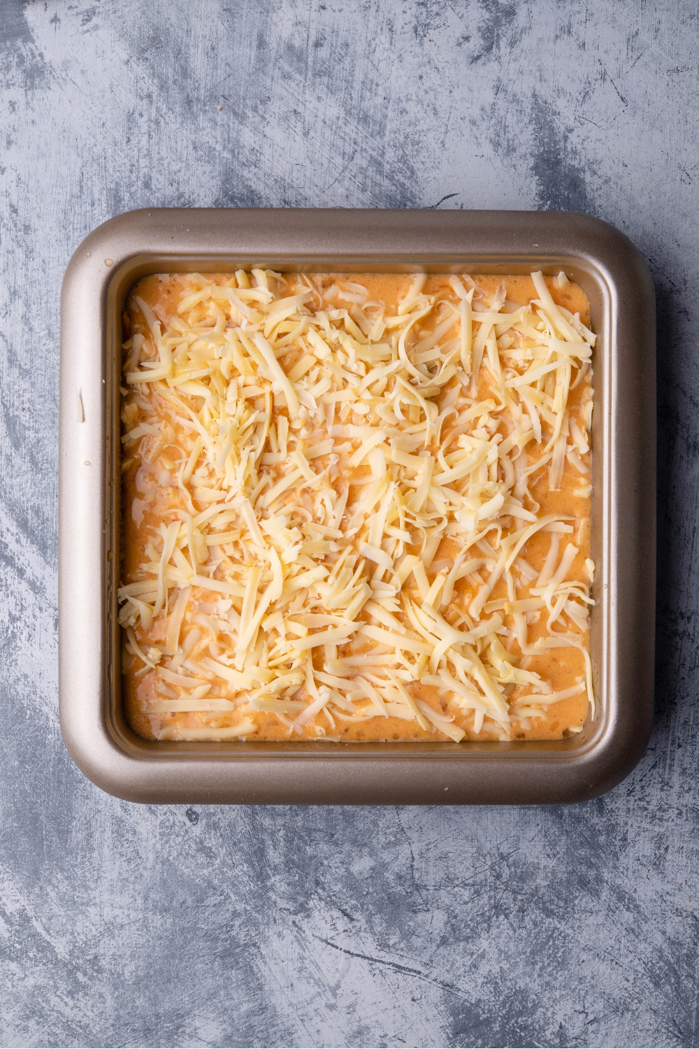 Unbaked chili relleno casserole in a square baking dish covered with shredded cheese.