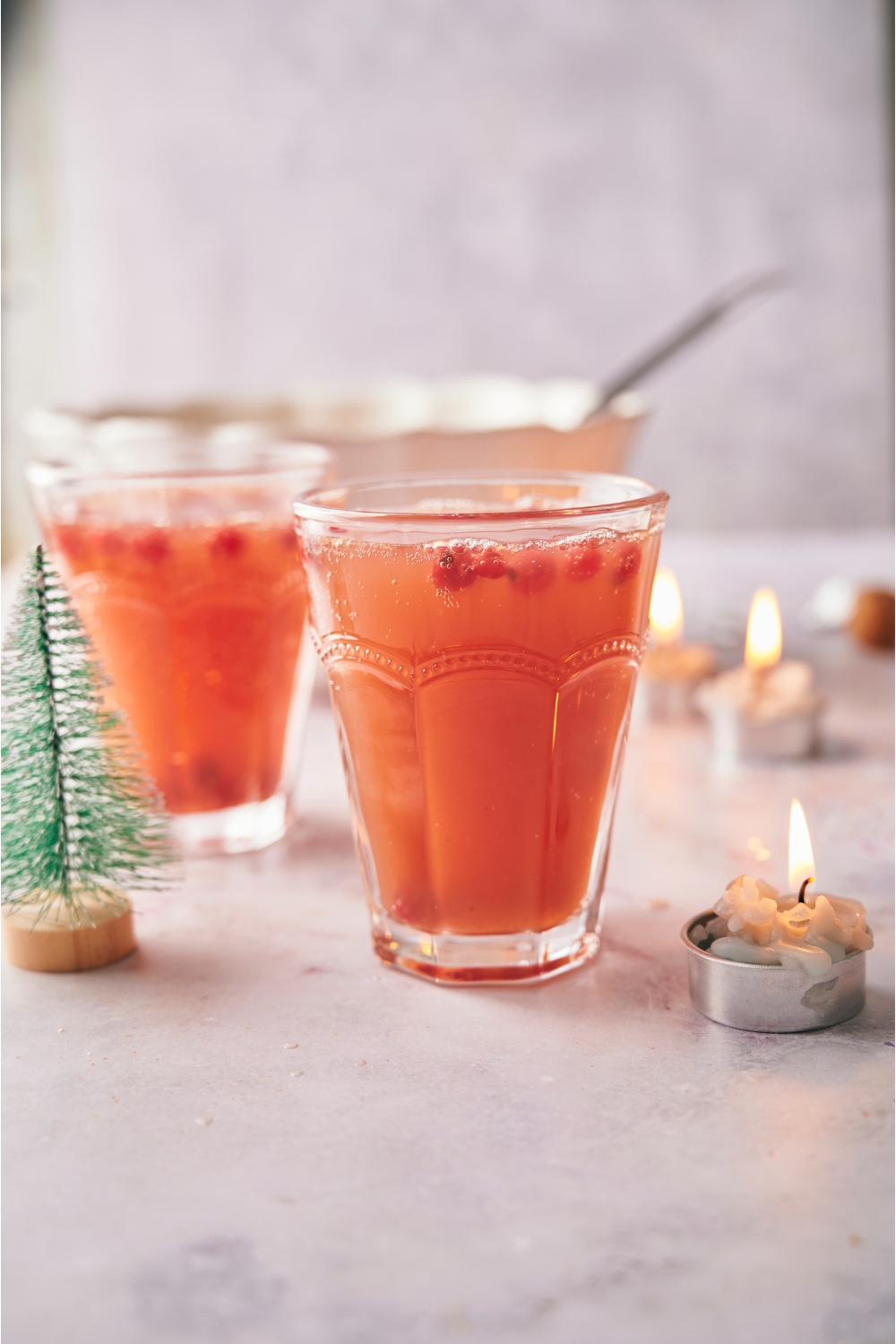 Holiday punch in a clear glass garnished with cranberries, a second serving of punch is in the background.