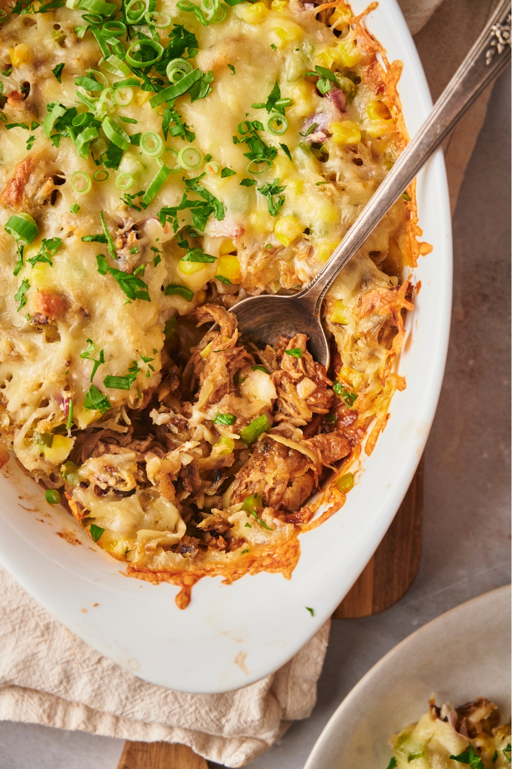 Pulled pork casserole in a white casserole dish with a serving spoon and a large serving missing from the casserole.