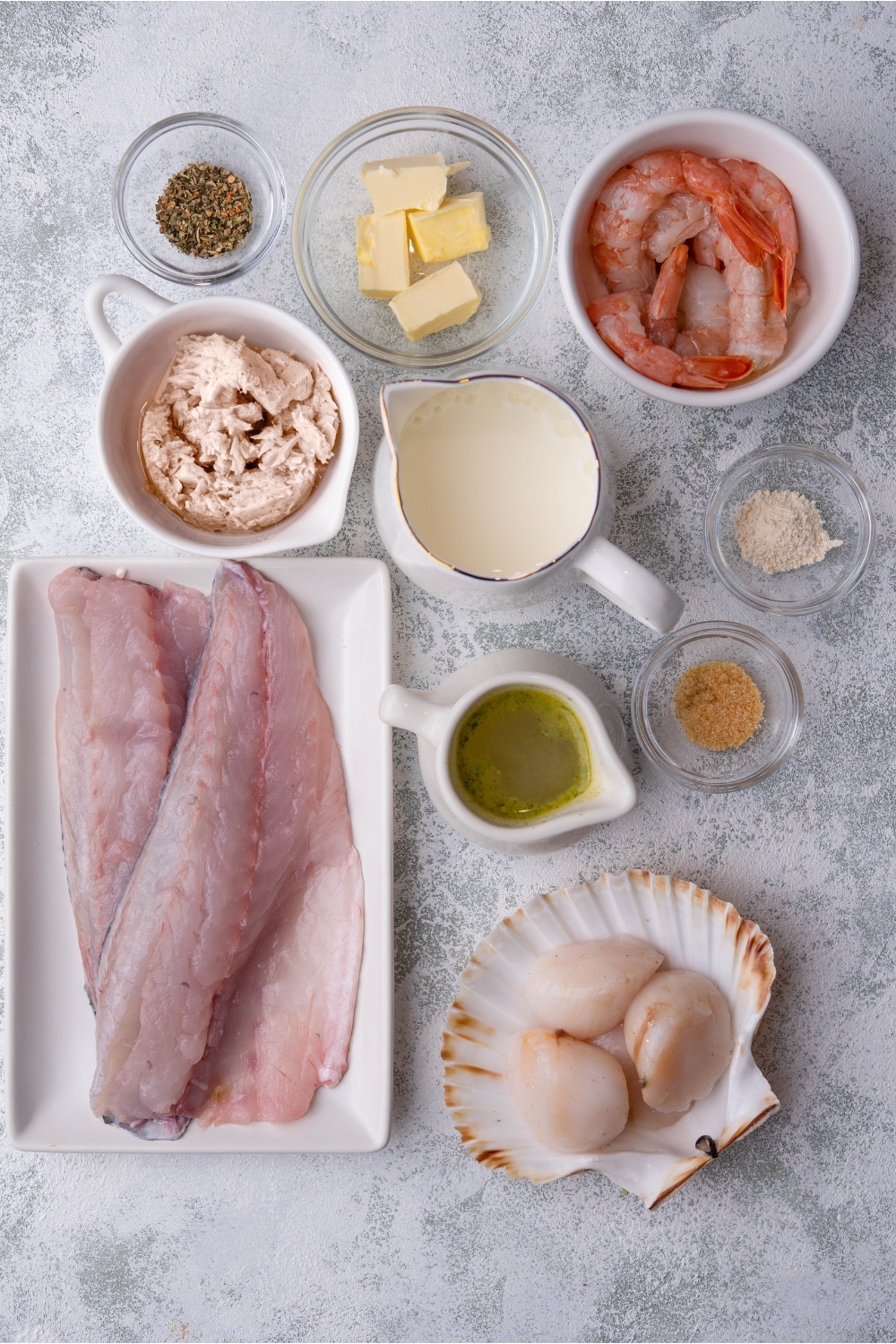 An assortment of ingredients including a plate of fish fillets and bowls of raw shrimp, scallops, crab meat, spices, butter, and cream.