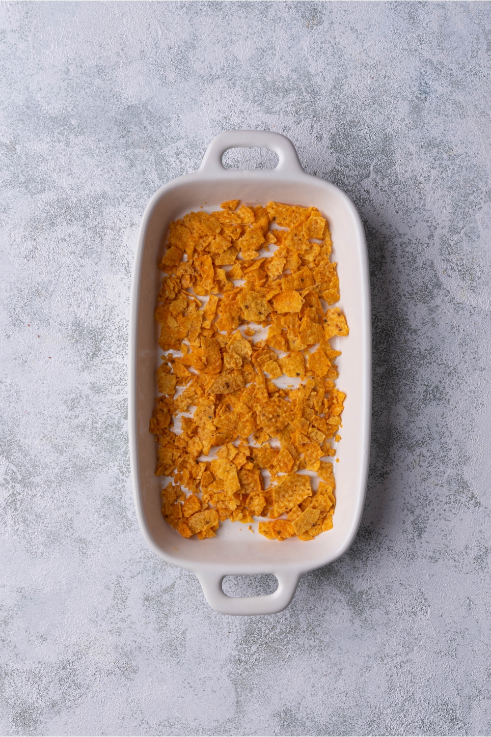 White baking dish with a layer of Dorito Nacho chips on the bottom.