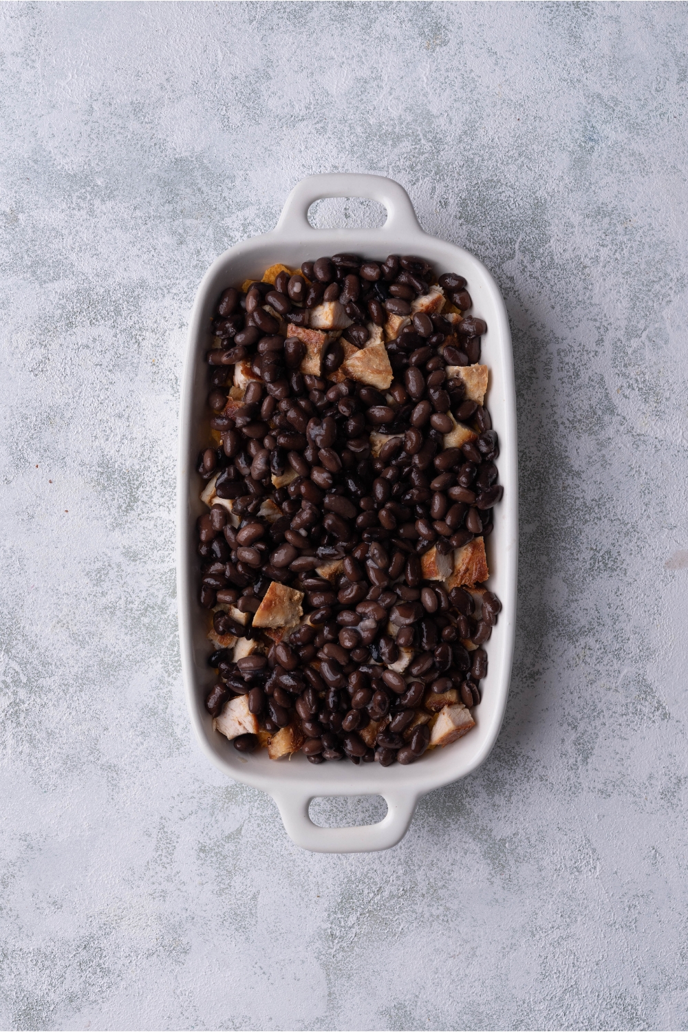 White baking dish filled with chicken and black beans.