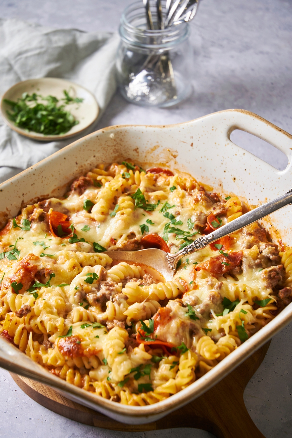 A deep baking dish with pizza pasta in it. A spoon is in it ready to serve.