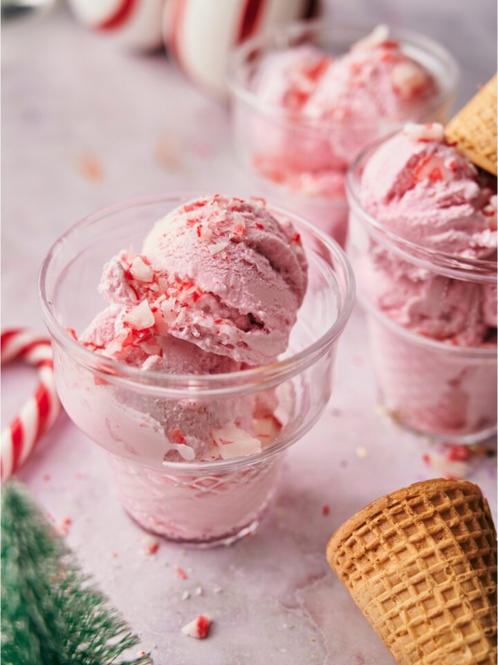 Peppermint ice cream in clear serving bowls, each topped with crushed candy canes and one topped with an ice cream cone.