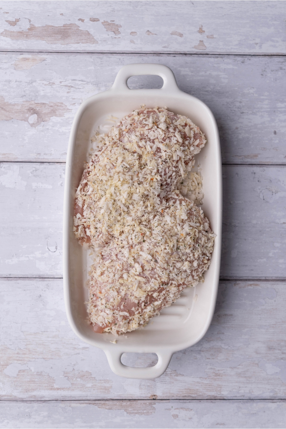 A white baking dish with two unbaked ranch chicken breasts.