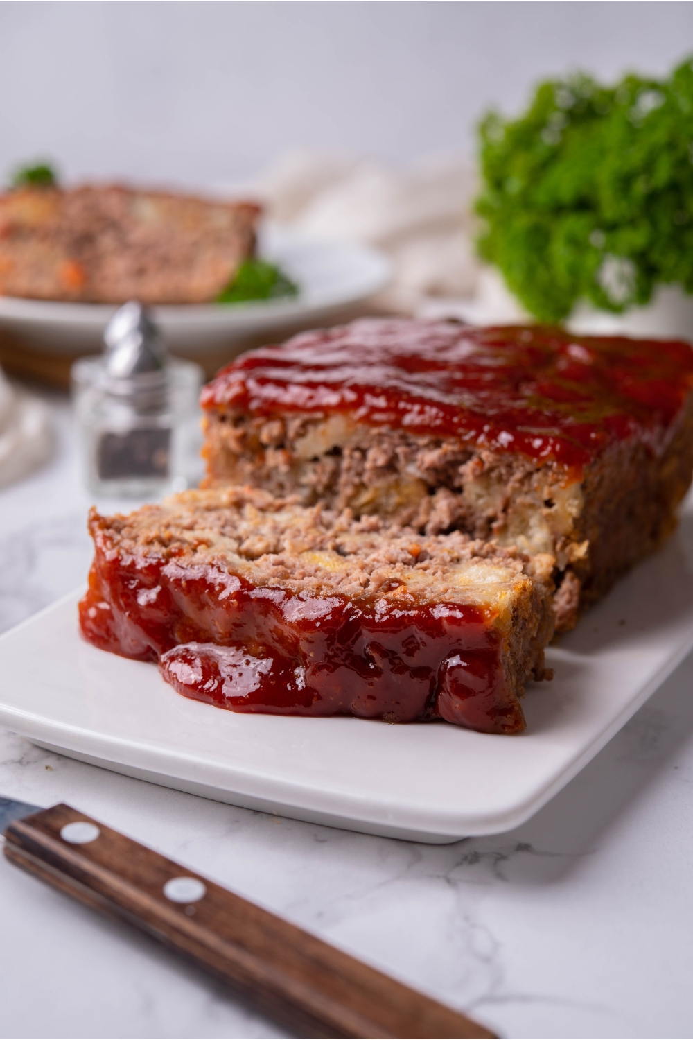 Meatloaf with stuffing on a white serving plate. One serving has been cut and is on the serving plate.