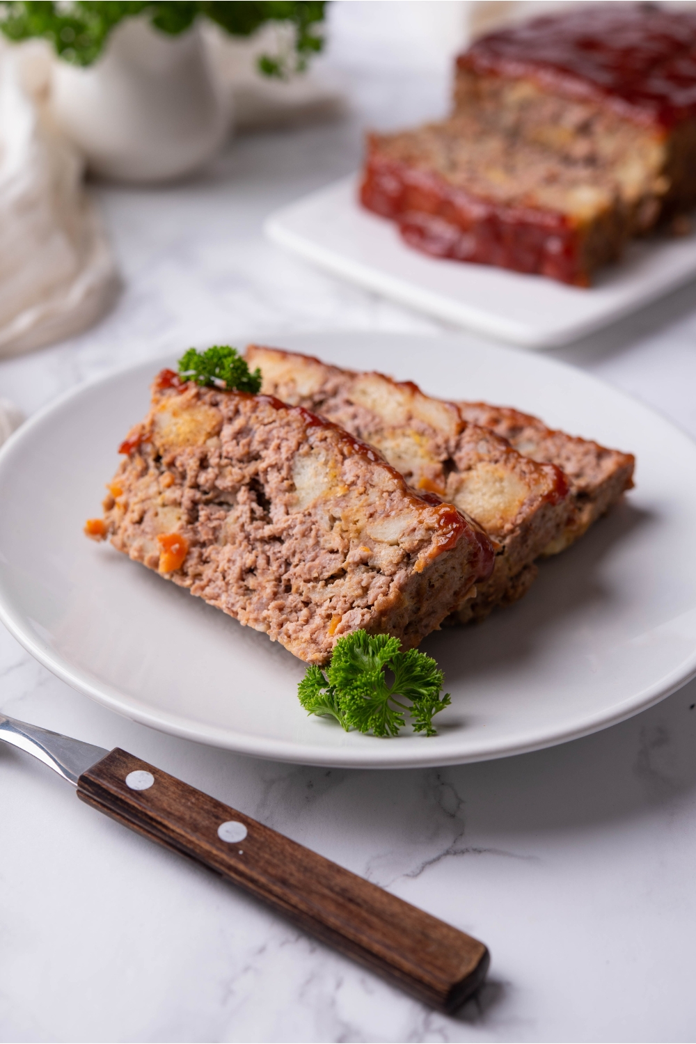Three overlapping slices of stuffing meatloaf garnished with parsley on a white plate.