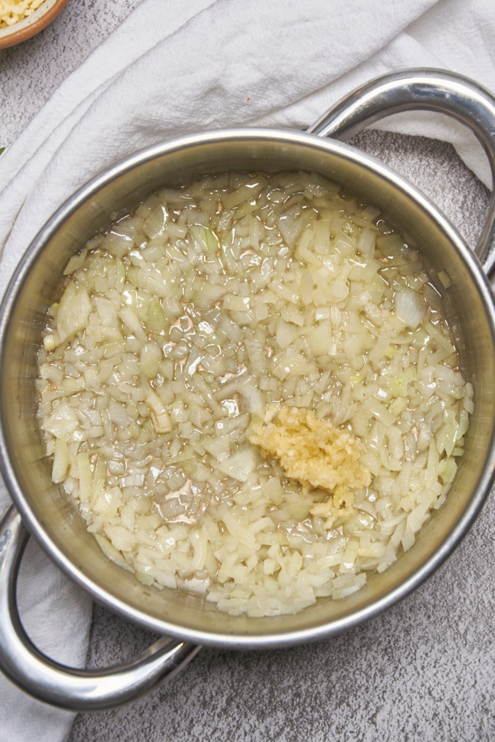 A deep pot with diced onions and minced garlic cooking.
