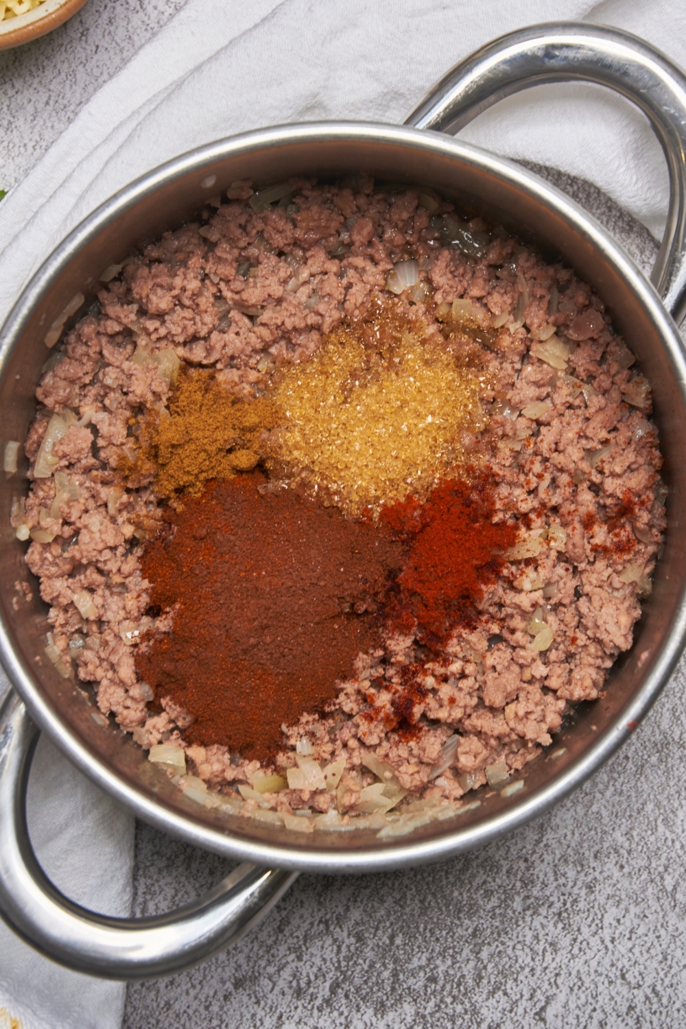 A deep pot with ground beef cooking. Seasonings have been added to it.